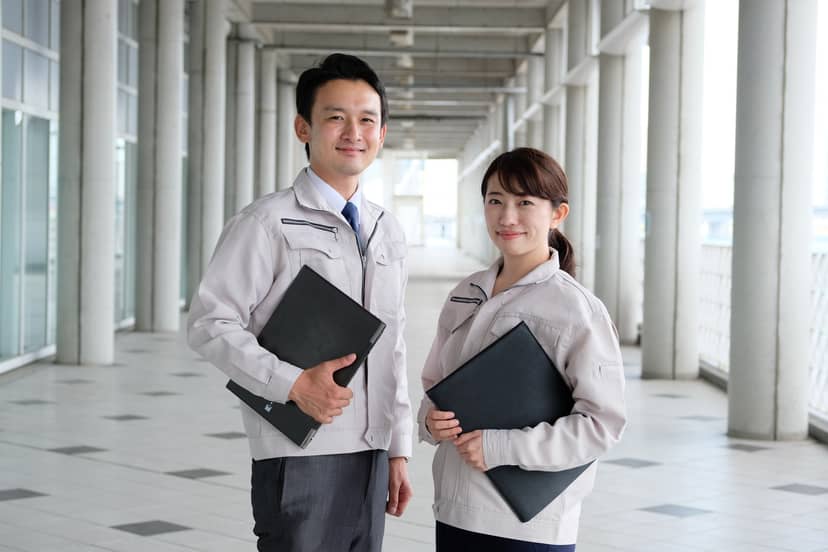 書類を持って立つ作業着姿の社員2名