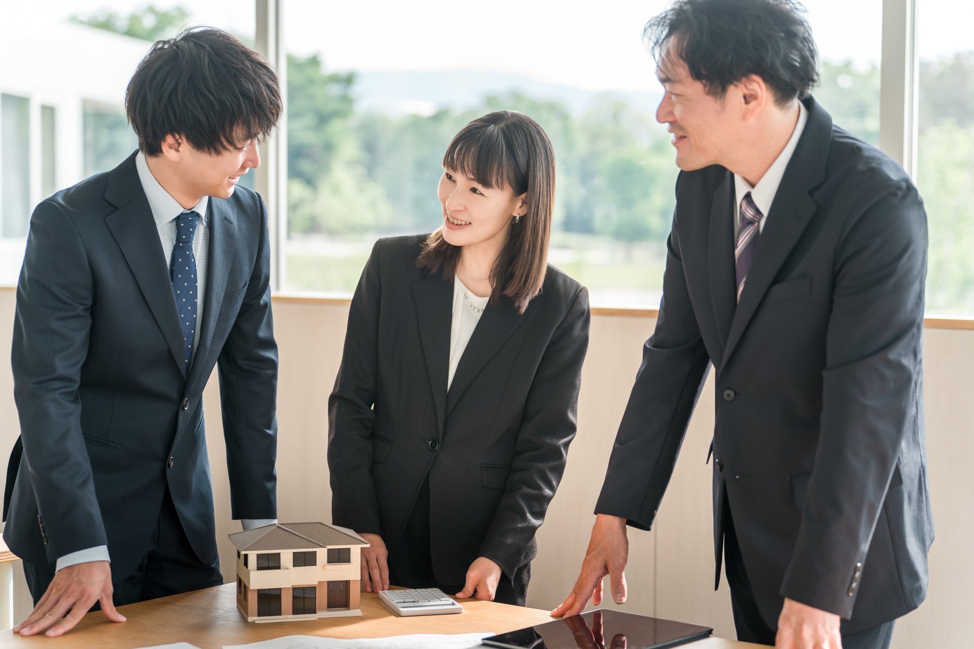住宅の模型と電卓を囲んで打ち合わせている3名